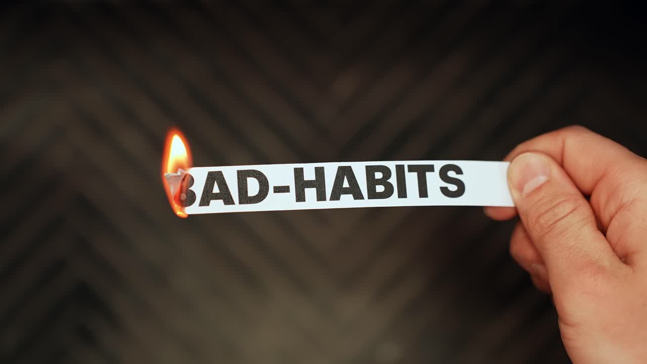 Hand burns a paper strip labeled BAD HABITS with a lighter, symbolizing quitting addictions, breaking routines, and personal change