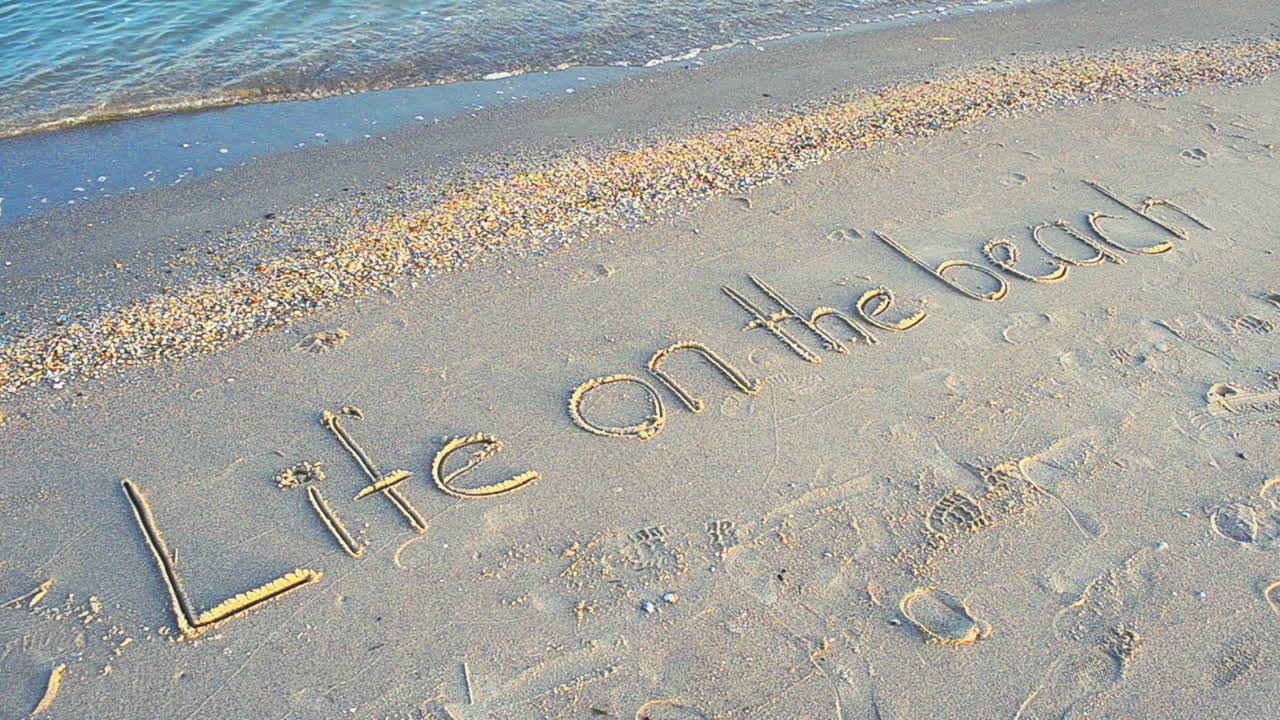 Optagelse på stranden. Livet på stranden-koncept – inskription i strandsand med en kommende bølge.
