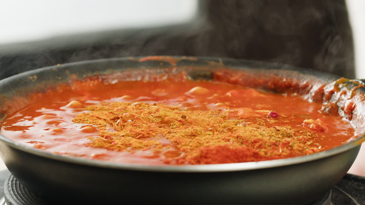 Chicken in tomato sauce is boiling on a frying pan with spices. Cooking tomato sauce curry with chicken fillet. Traditional Italian Mexican Asian dish. High quality studio shot for cafe, restaurant close up.