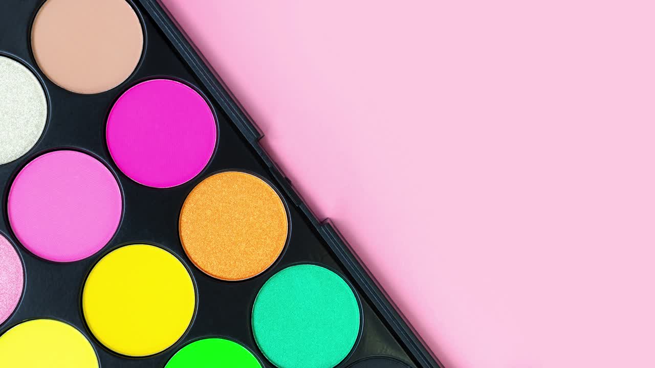 Multicolored beautiful neon eyeshadow palette on trendy pastel pink background. Beauty products. Makeup cosmetic. Summer eye shadow. Yellow, green. Bright colorful stop motion animation. Looping video