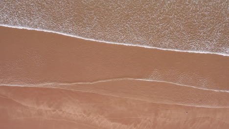 aerial truck shot of ocean waves lapping against a sandy golden beach