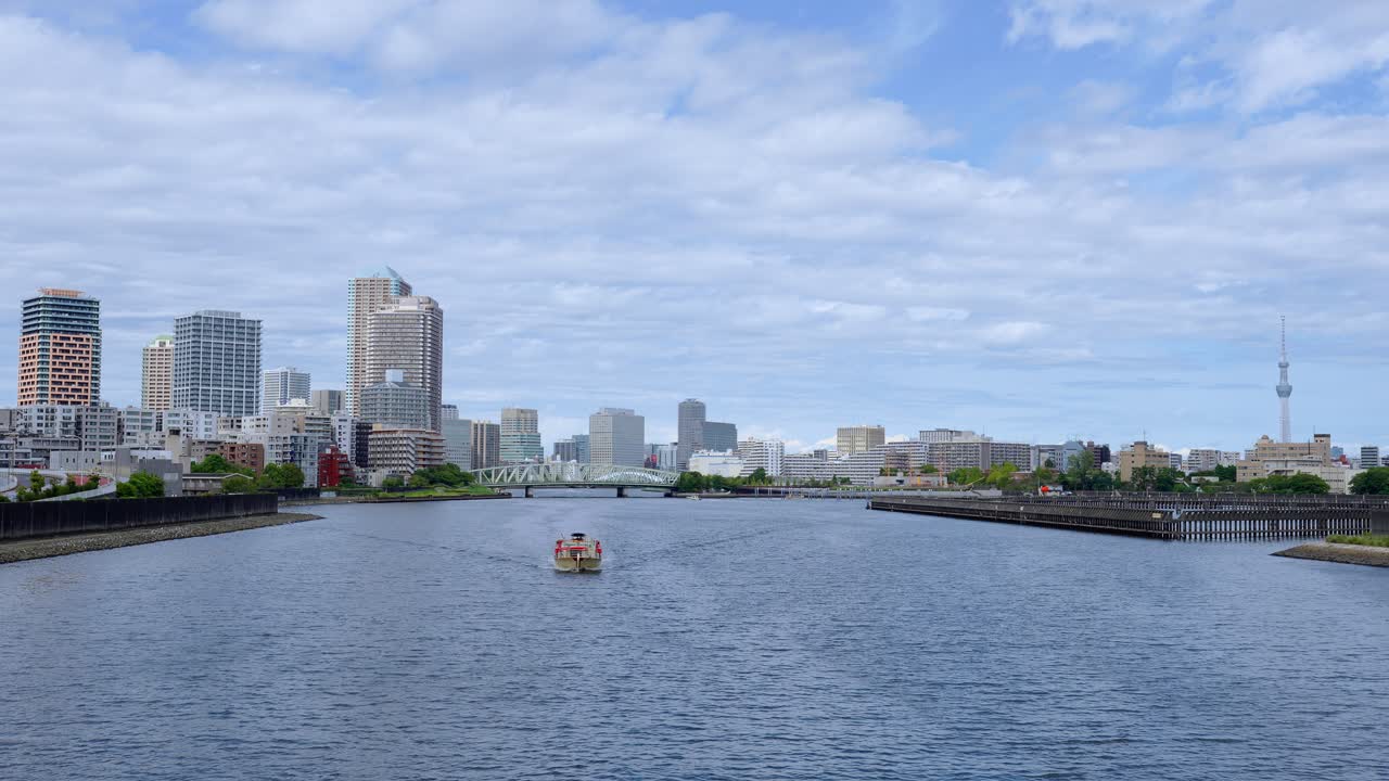 A peaceful shot of two boats traveling down a river with the Tokyo cityscape and modern buildings in the background