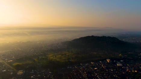 Monte-Tidar-En-El-Pintoresco-Amanecer-Y-La-Ciudad-De-Magelang-Cubierta-De-Niebla,-Vista-Aérea