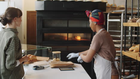 woman buying fresh bread and paying with smartphone in bakery