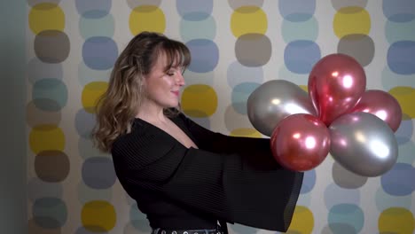 mujer joven posando y sosteniendo globos en la mano contra un fondo colorido