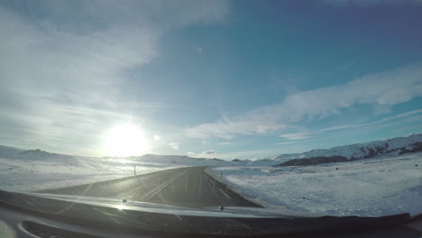perspective from the windshield on a road trip through the snowy icelandic mountains driving towards the sunset