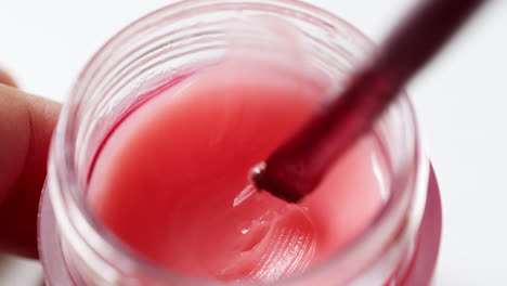 mezclar un brillo de labios rosa húmedo con un pequeño aplicador en un recipiente, en preparación para una aplicación de maquillaje completo