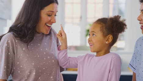 Family-With-Two-Mums-Wearing-Pyjamas-Making-Morning-Pancakes-In-Kitchen-At-Home-With-Daughter