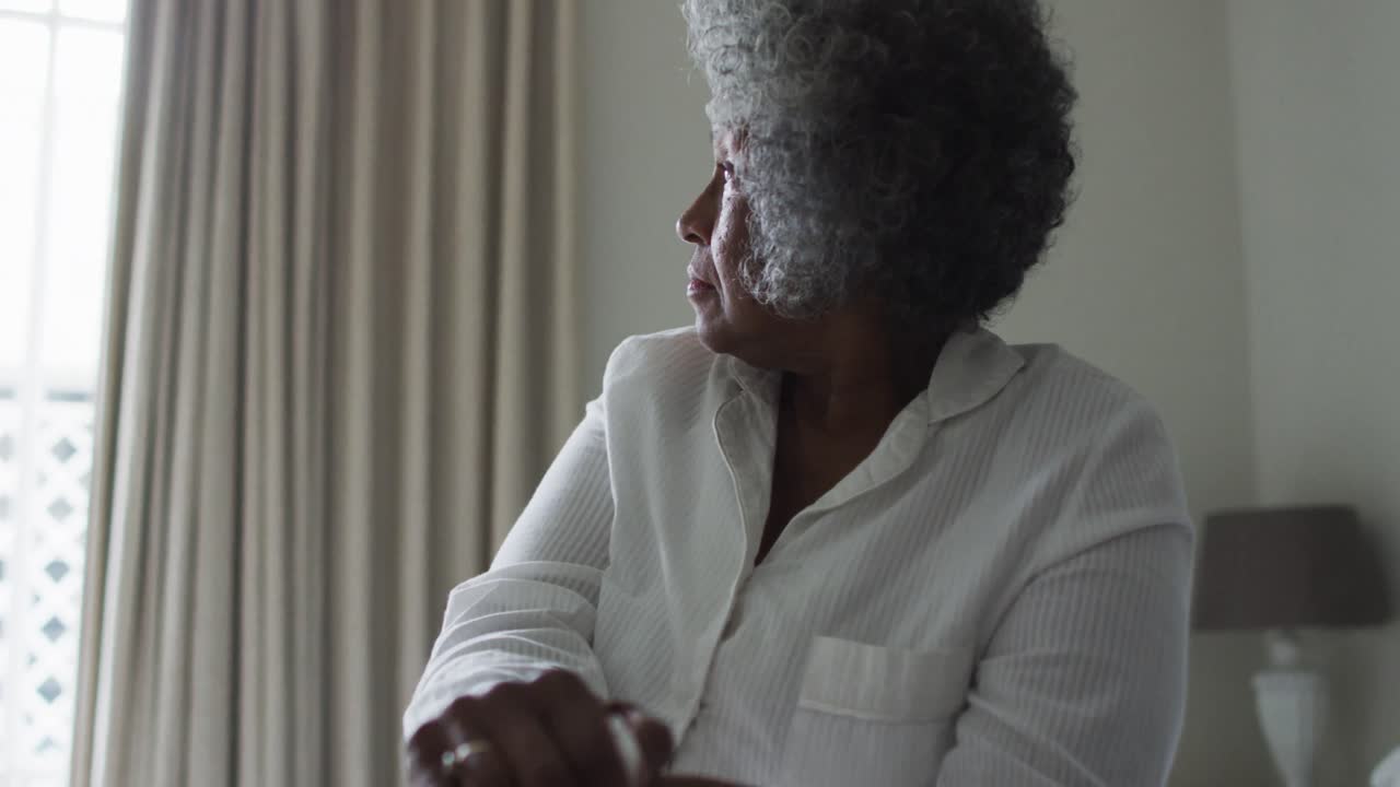 Anziana donna afroamericana che tiene un bastone da passeggio seduta sul letto a casa.