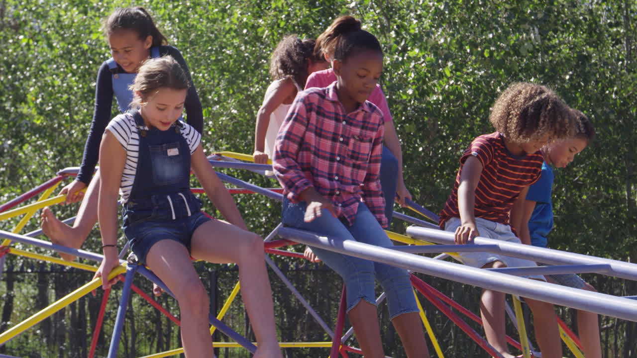 Pre-teen friends climbing off climbing frame in a playground