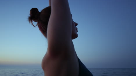 profile girl raising hands to dark sky close up. woman practicing yoga on beach.