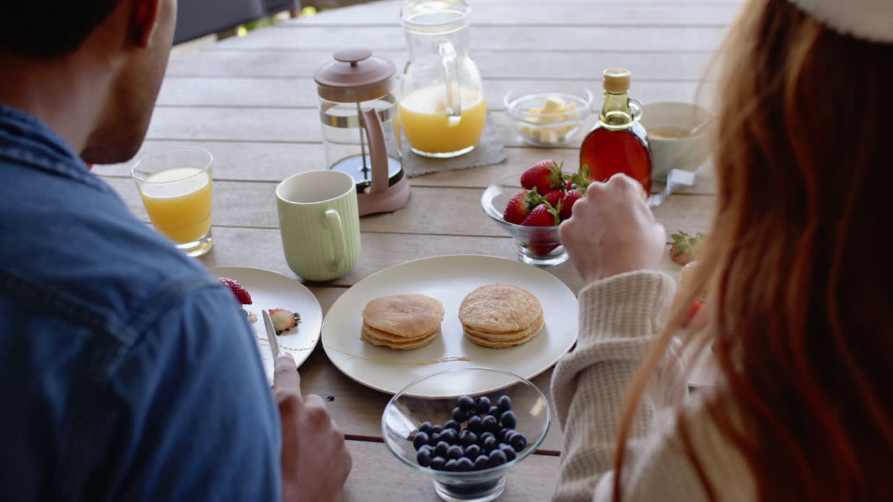 Christmas time, Diverse couple enjoying festive breakfast with pancakes and fresh fruit outdoors