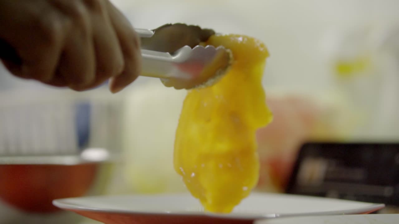 Primer plano de una mano sirviendo comida de color amarillo brillante con pinzas de cocina.
