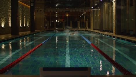 man swimming in an indoor pool at night