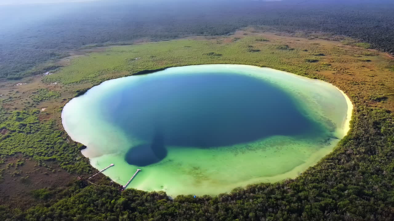 Aerial drone view of Kaan Luum Lagoon circular cenote surrounded by tropical jungle in Tulum, Mexico, showing deep blue center and shallow turquoise water