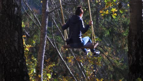 brunette girl swings in forest trail rope swing in sunny autumn day