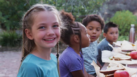 retrato de una niña sonriente con amigos comiendo un picnic saludable en una mesa al aire libre en el campo