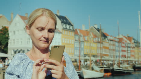 Eine-Glückliche-Frau-Benutzt-Ein-Smartphone-Steht-Vor-Dem-Hintergrund-Des-Kanals-Und-Der-Beliebten-Touristenstraße