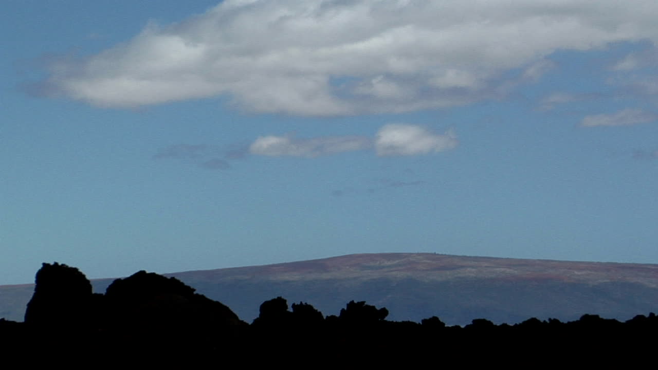 검은 용암 흐름 뒤에 저지대 화산이 보입니다.