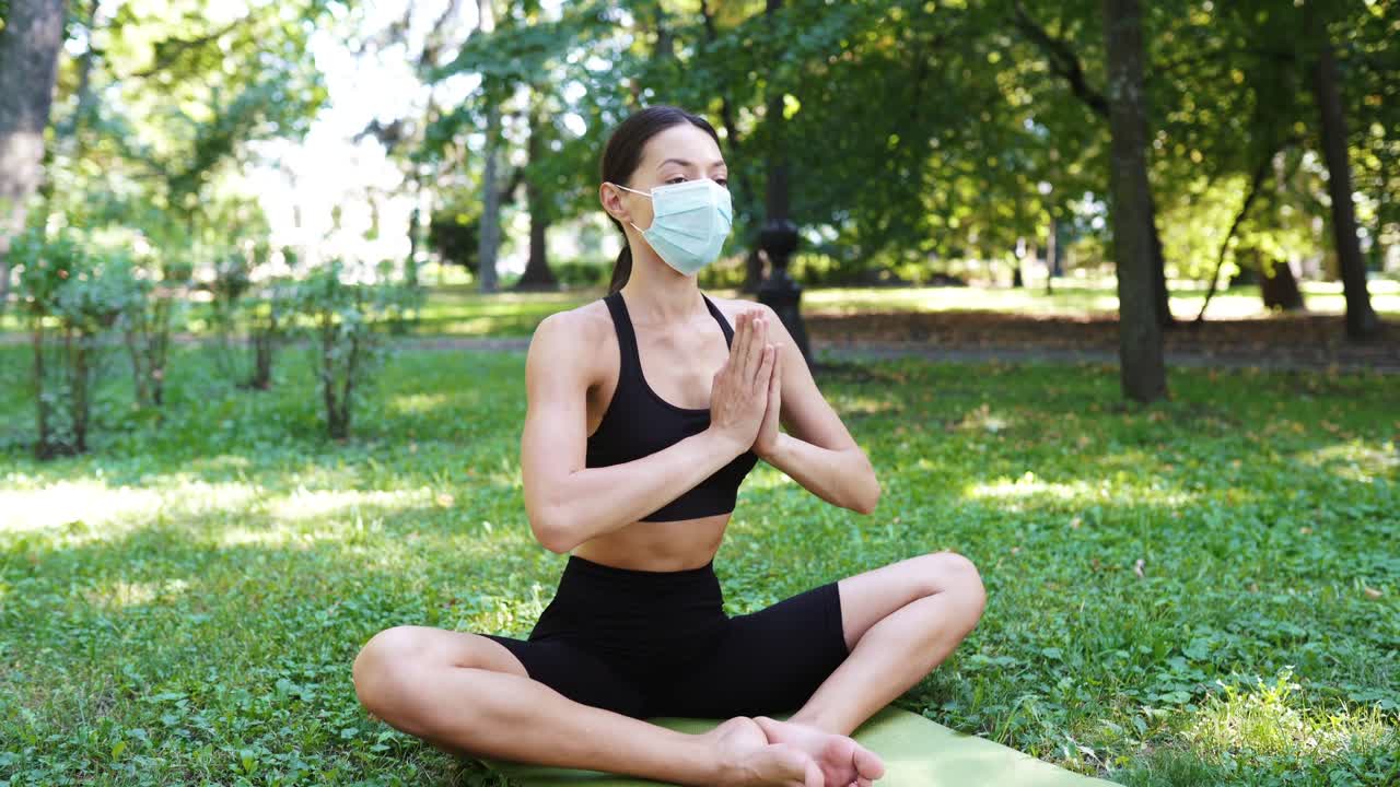 얼굴 마스크 를 착용 한 공원 에서 요가 를 연습 하는 여자