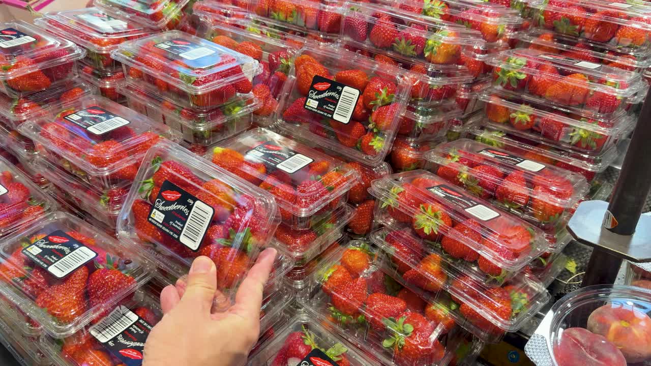 Una persona prende ed esamina una confezione di fragole in un negozio di alimentari