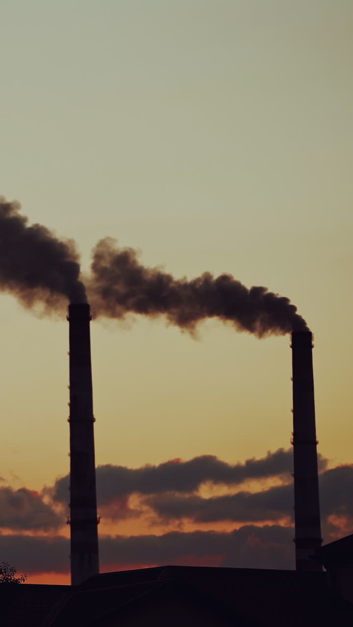 Air pollution. Industrial pipes with thick smoke pollute the atmosphere. Two big pipes with toxic smoke on the natural background in the evening. Vertical video