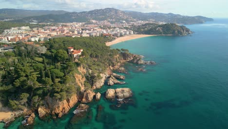 Erleben-Sie-Den-Charme-Der-Luftlandschaft-Von-Lloret-De-Mar-Mit-Ihrem-Azurblauen-Meer,-Den-Sandstränden-Und-Exklusiven-Sehenswürdigkeiten-Wie-Santa-Cristina-Und-Cala-Treumal