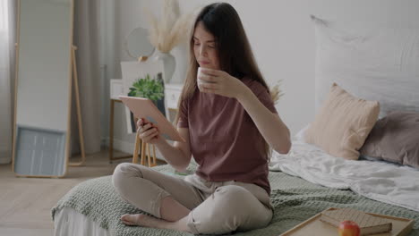 woman relaxing in bedroom with tablet and coffee