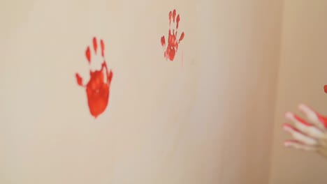 Happy-cute-little-boy-is-having-fun-leaving-his-red-handprints-on-the-wall.-Young-happy-family.-Mother-and-child-concept