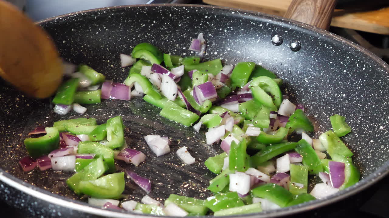 Cooking green peppers and red onions in frying pan at home, closeup