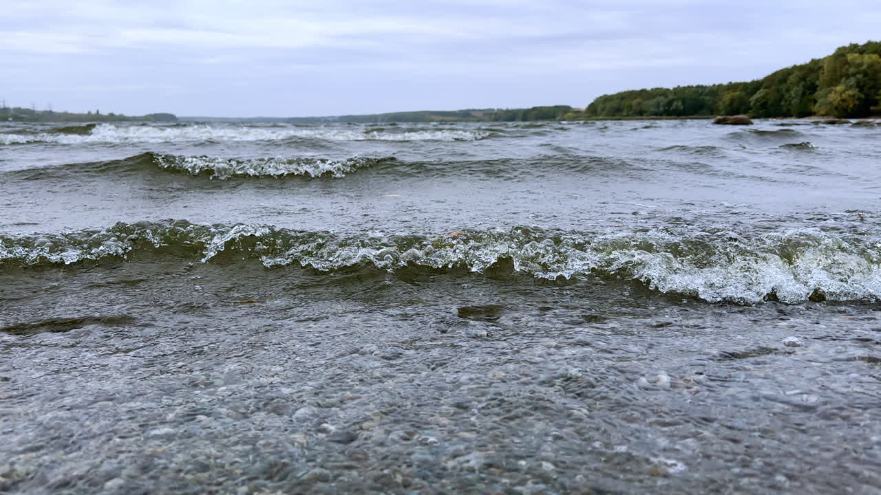 Little waves on the river rolling to the shore. Forest growing on the waterfront at backdrop.