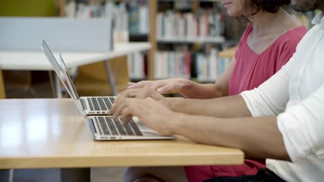 side view of students typing on laptops at library