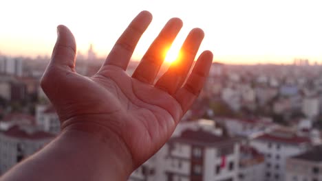 hand reaching for the sunset over a city