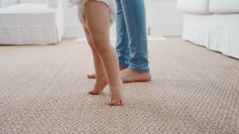 Bebé-Dando-Sus-Primeros-Pasos-Niño-Pequeño-Aprendiendo-A-Caminar-Con-La-Madre-Ayudando-Suavemente-Al-Bebé-Enseñándole-Al-Niño-En-Casa-Confianza-En-La-Maternidad