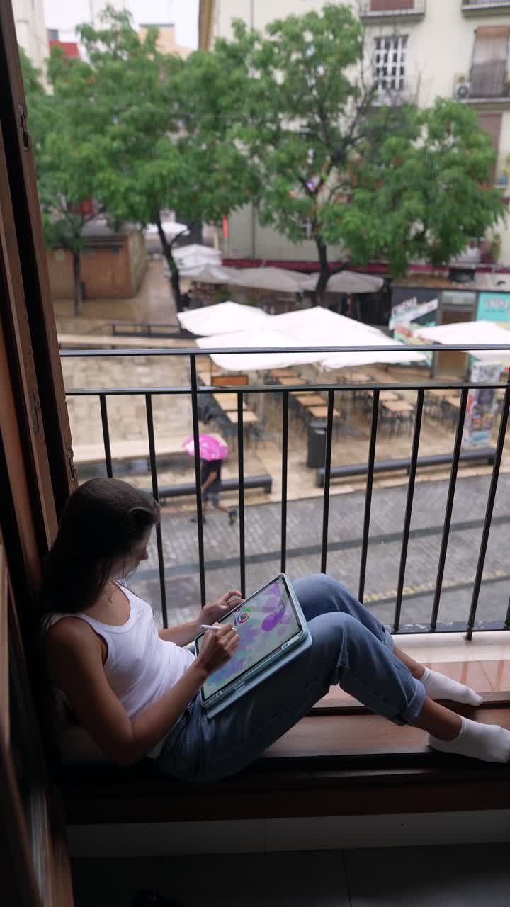 mujer dibujando en una tableta en un café de la ciudad lluviosa