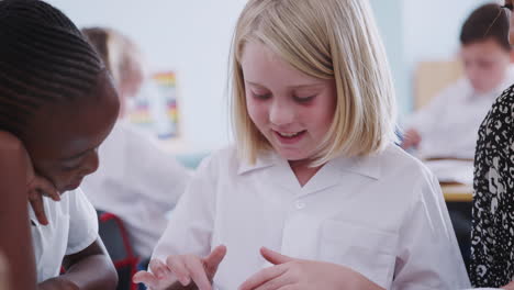 Female-Teacher-With-Two-Elementary-School-Pupils-Wearing-Uniform-Using-Digital-Tablet-At-Desk