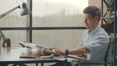 architect man standing working with blueprints sketching a construction project on wood desk at home office.construction design concept.vintage color tone. engineer works in a bright office with a large window concentrates and draws blueprints. workplace of an architect or designer: loft style minim