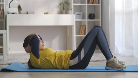 home fitness and workout young woman is doing physical exercise for abdominal muscles lying on floor and lifting torso side view on body