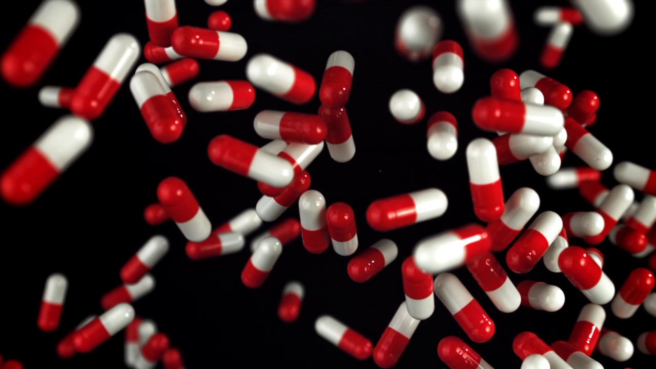 Capsule mediche rosse e bianche che cadono al rallentatore su sfondo nero