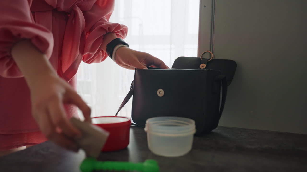Woman Organizes Belongings Before Leaving House, Woman Effortlessly Arranges Her Items In Handbag Near Doorway, Female Prepares Her Small Container And Handbag Efficiently For Quick Departure