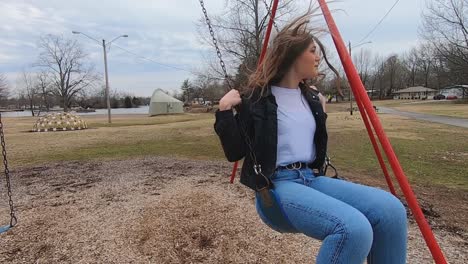 60 fps footage of a beautiful brunette college teenager swinging on a swing set in a city park