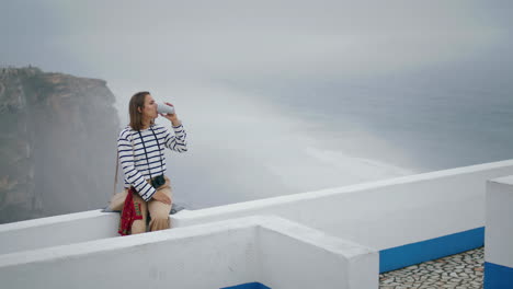 relaxed tourist drinking coffee at seaside view vertical. girl enjoy vacation