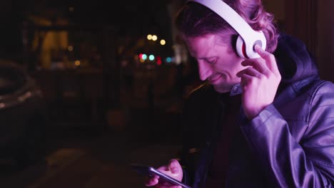 caucasian hooded male wearing headphones, smiling, lying on the wall, in the evening