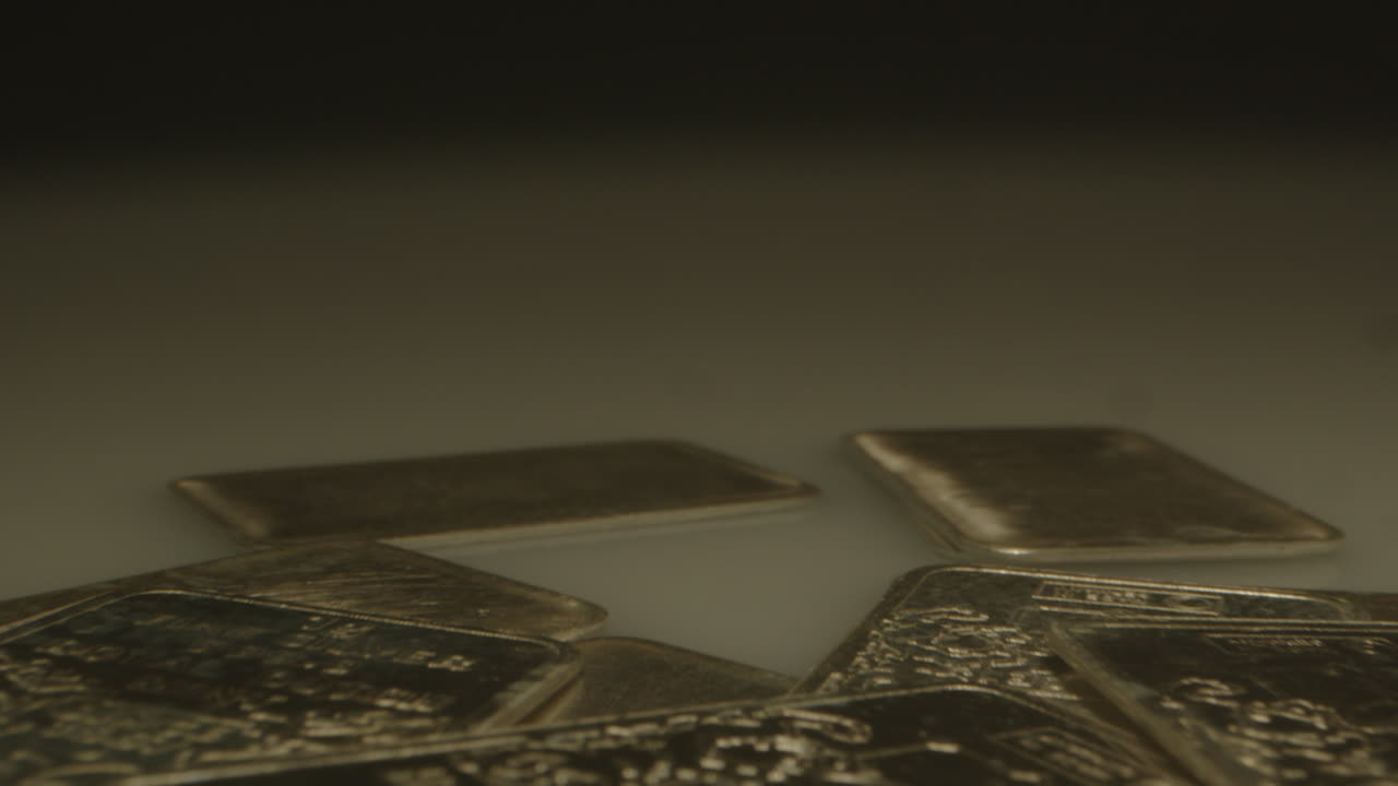 Beautiful macro dolly in of a lot of silver bars spread over a white surface. The camera moves over the pure silver plates