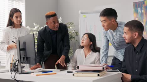 group of organized helpful creative ambitious people spend time in company on common project, they talk, discuss, brainstorm, stare at computer screen, young guy in suit points and explains