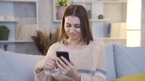 mujer joven sentada en el sofá comprando en línea o usando las redes sociales en su teléfono inteligente.