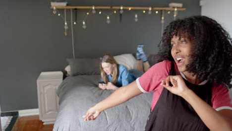 happy diverse female friends using smartphone and dancing at home, slow motion