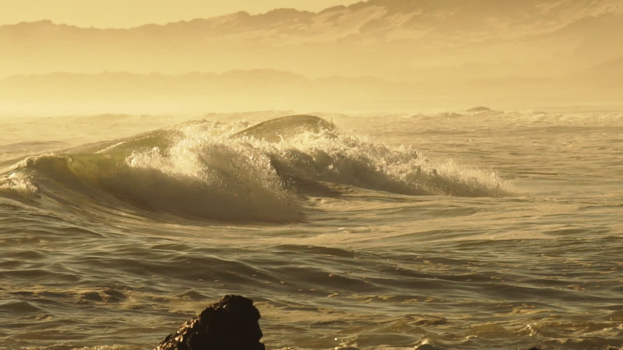 olas violentas del mar chocando contra la costa rocosa durante la tarde dorada - toma de medio plano