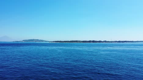 Peaceful-blue-sea-panorama-around-low-lying-tropical-island-with-trees-forest-under-clear-bright-sky-in-Indonesia