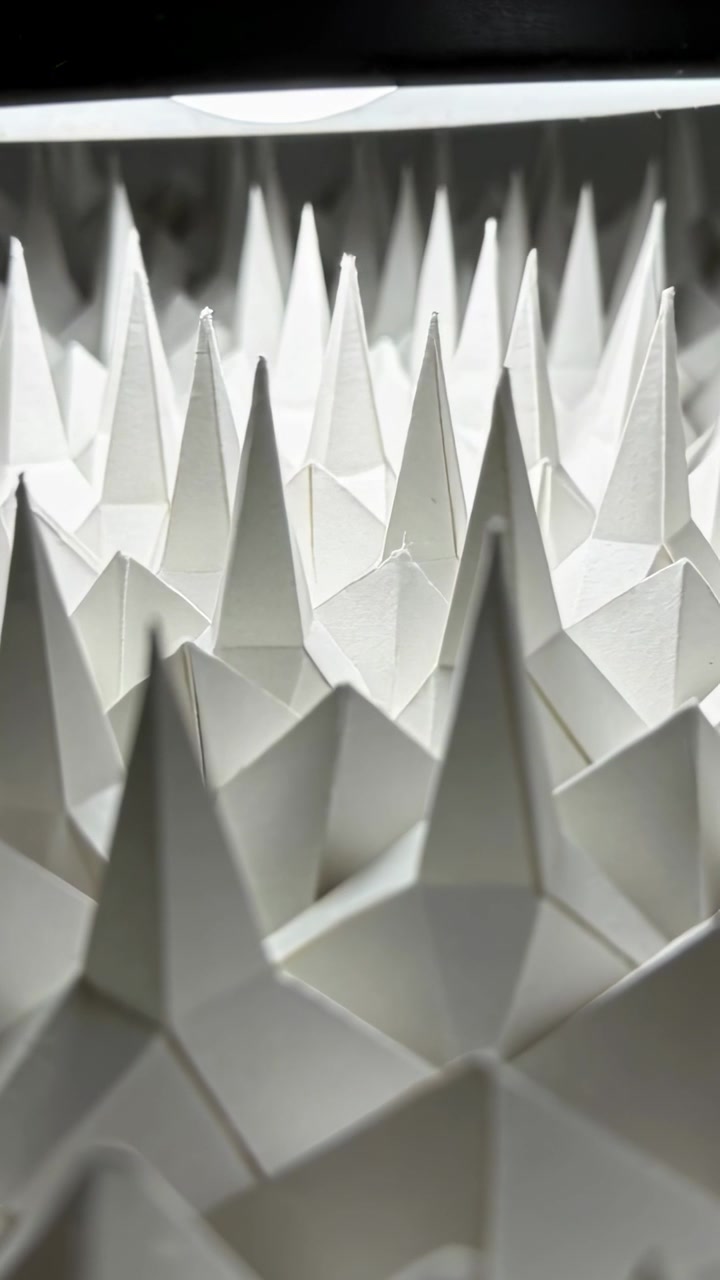Vídeo vertical: Câmera deslizando e inclinando pela tela para destacar pontas de origami sob luz de contorno.